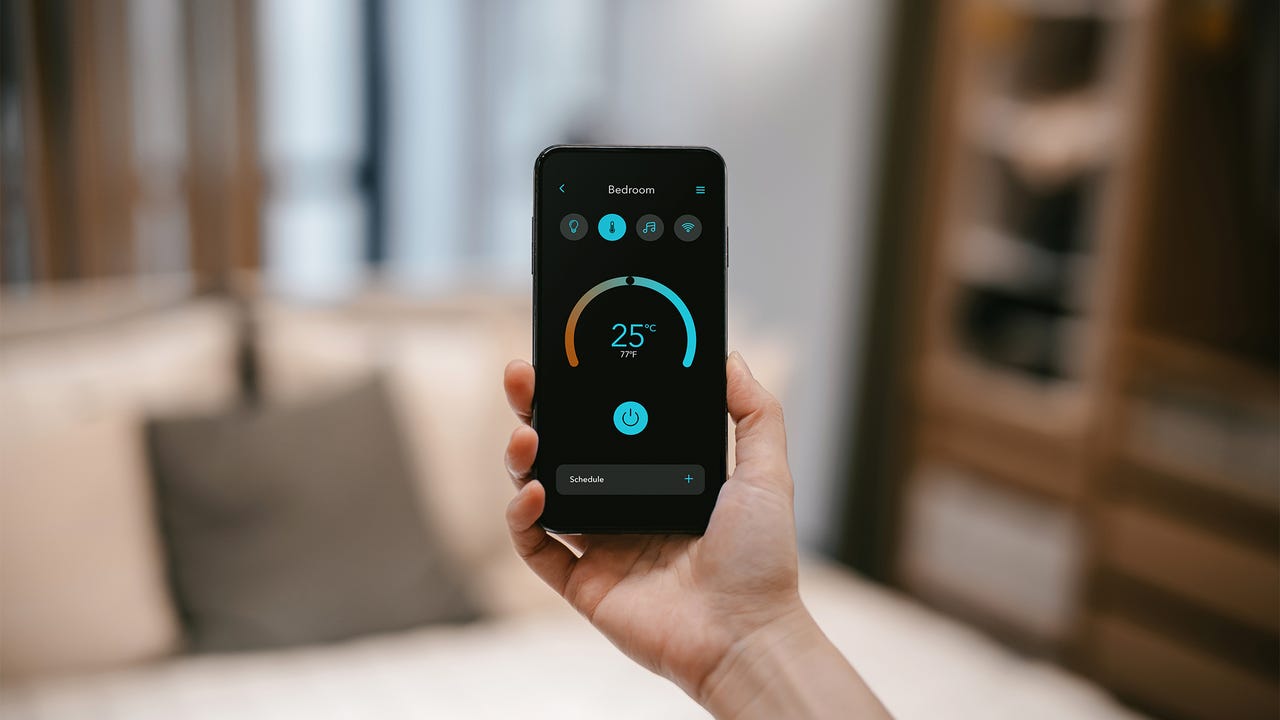 Closeup of woman's hand holding smartphone and setting up intelligent home system, remote-controlling the thermostat of smart air-conditioner in the living room of her smart home. Smart living. Lifestyle and technology - stock photo
