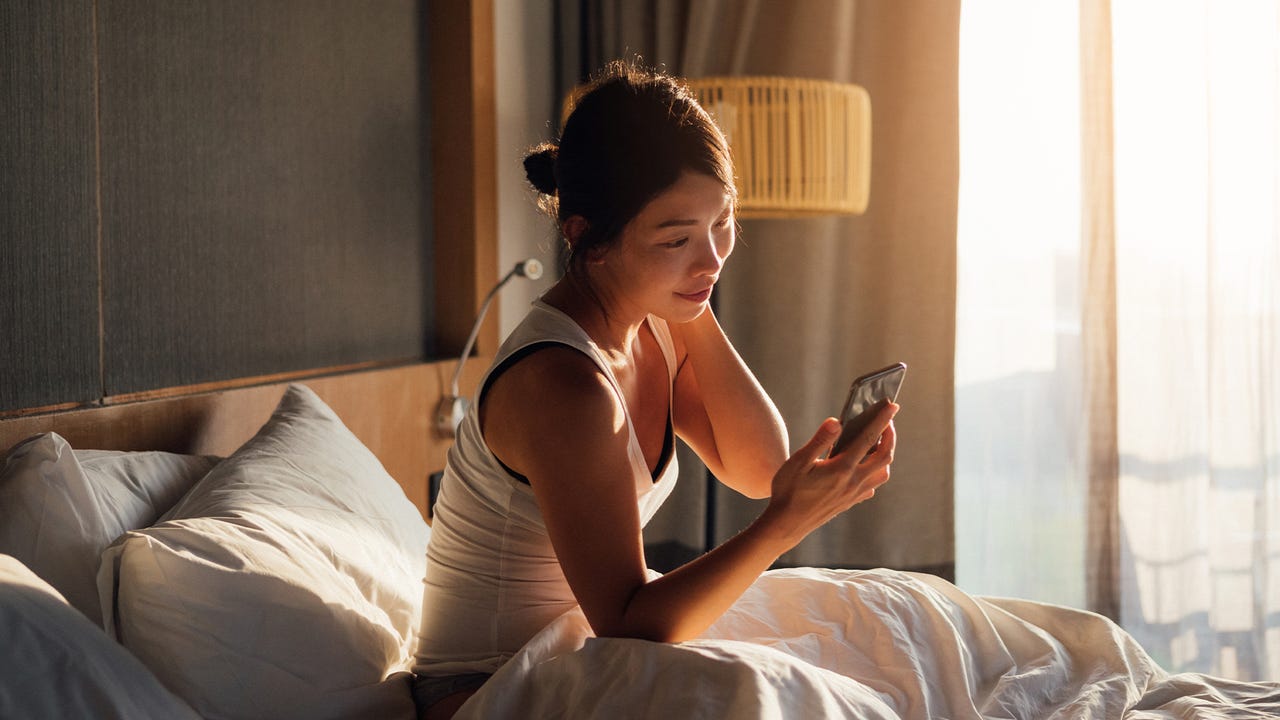 Young Asian woman holding smartphone while waking up in bed in the morning.
