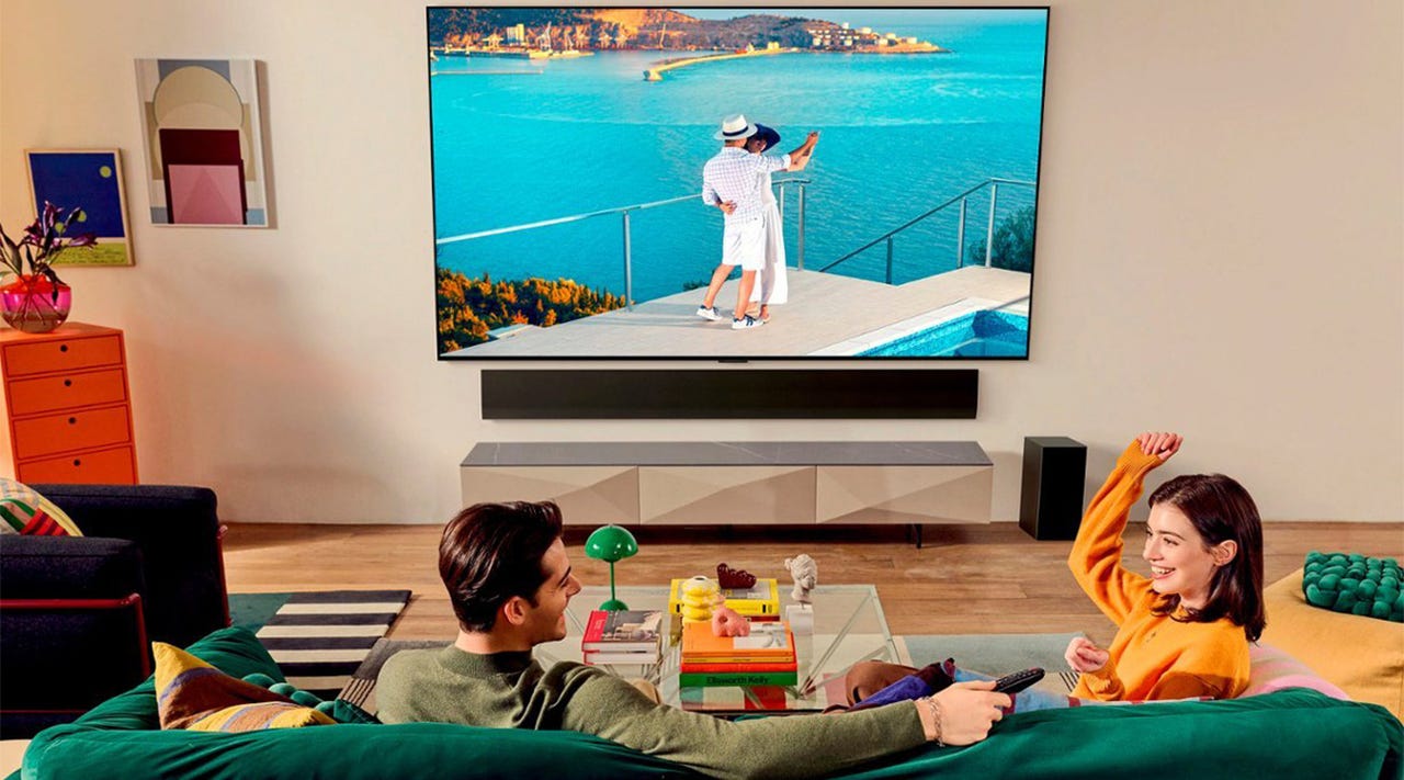 A from-behind view of a man and woman on a couch, watching a movie on an LG OLED TV